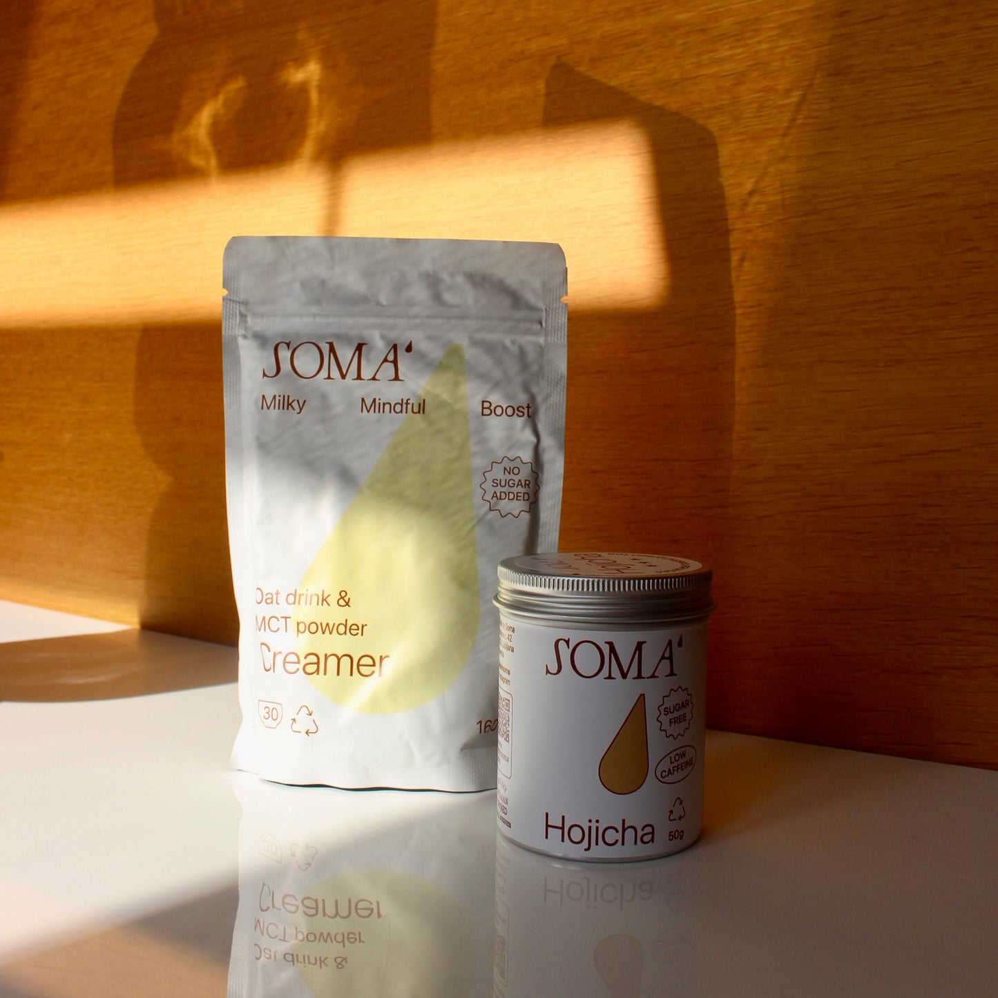 SOMA oat drink and MCT powder package with a soma hojicha tin on a white table.