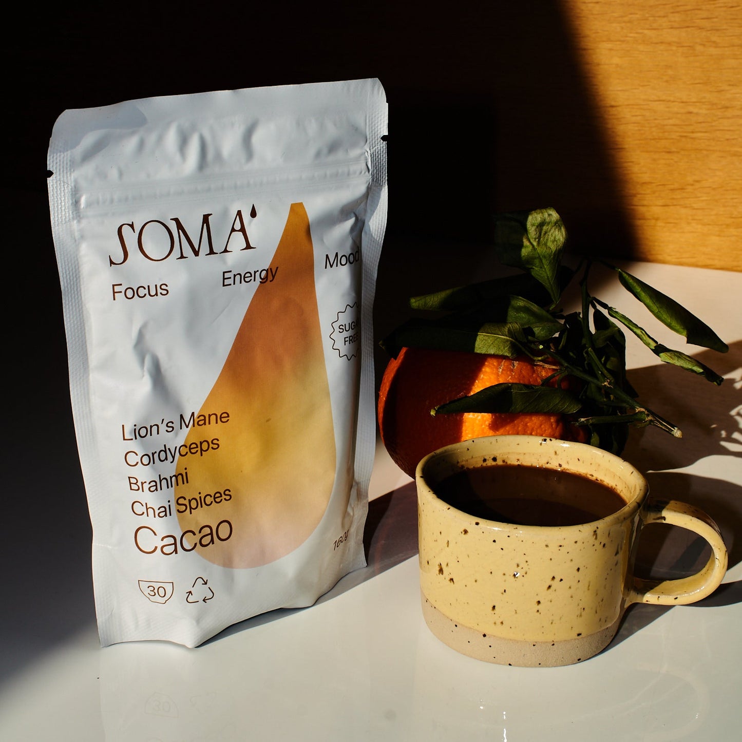 SOMA product packaging with a mug and an orange on a white table.