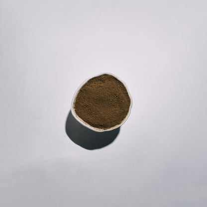 Small white container with dark brown hojicha powder on a light gray background