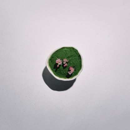 Small round container with green matcha and pink flowers on a white background