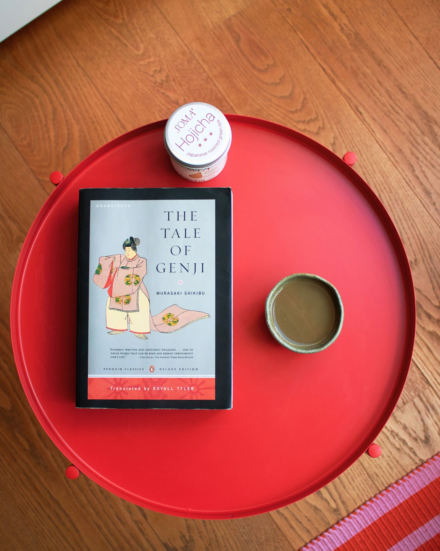 Book titled 'The Tale of Genji' on a red surface with a small cup and soma hojicha tin.
