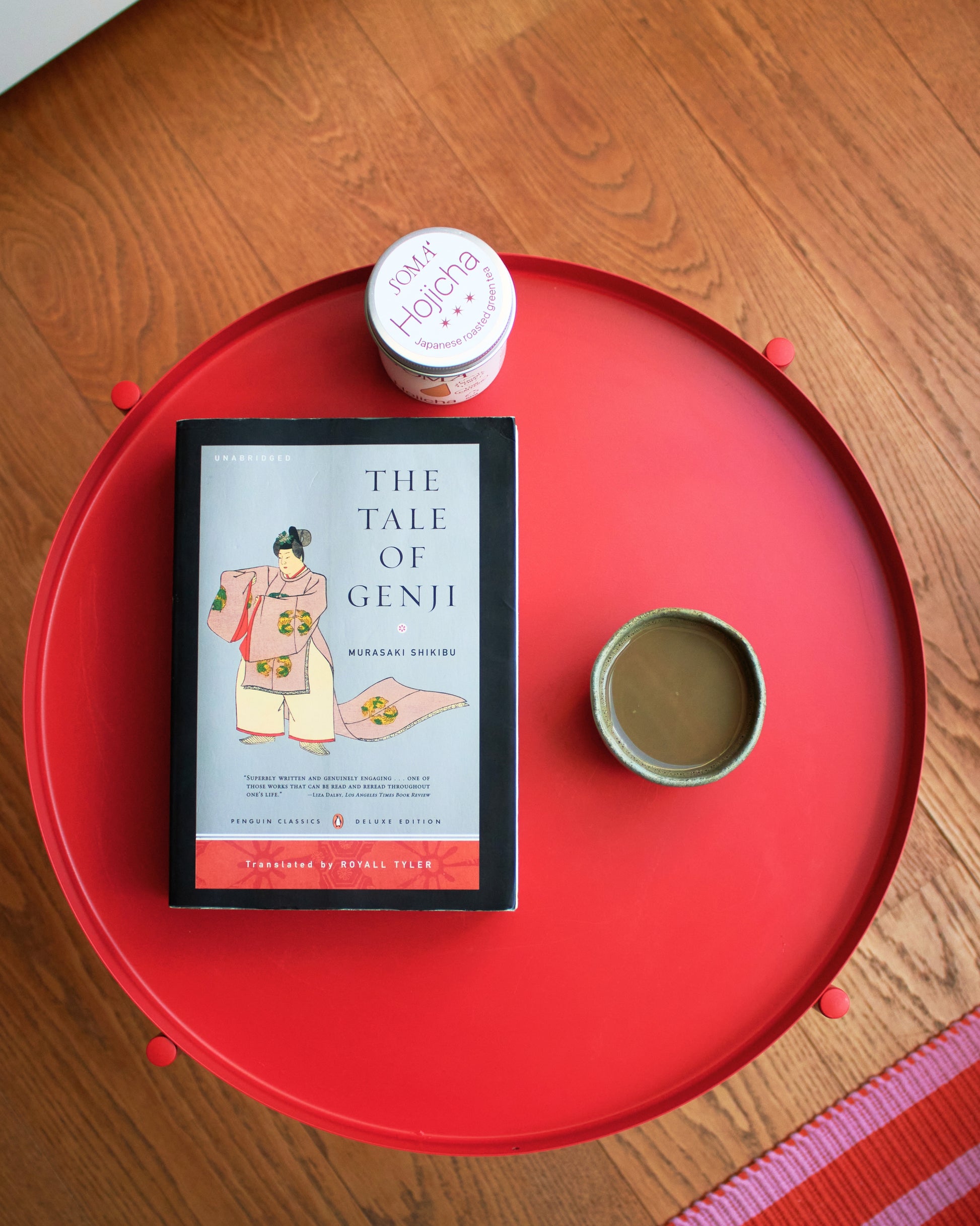 Book titled 'The Tale of Genji' on a red surface with a small cup and soma hojicha tin.