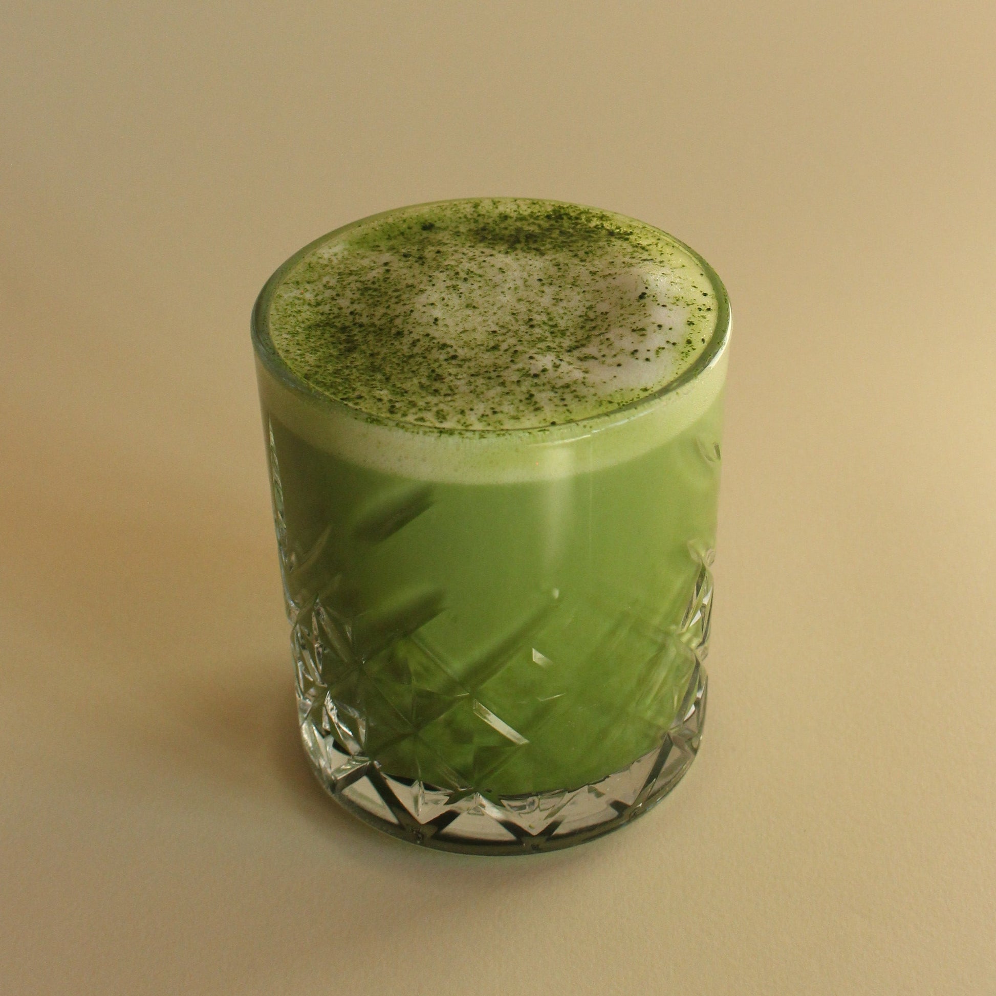 Matcha latte in a glass with a textured surface on a beige background