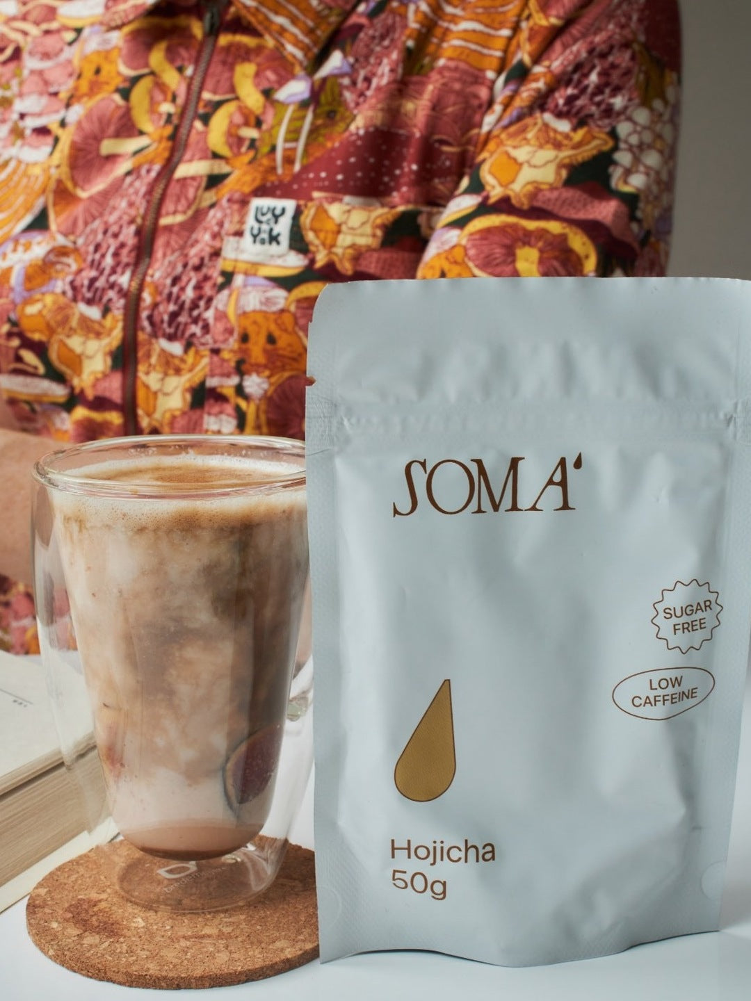 Soma Hojicha pouch with an iced hojicha latte in a glass on a cork coaster